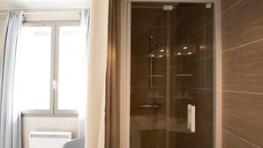 A modern bathroom with a glass shower enclosure, a white radiator, and a window with curtains. - Le Jostel 2 (Genay)