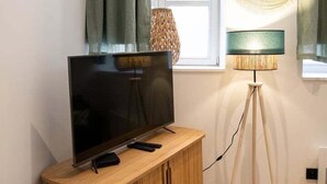 A modern living room with a flat-screen TV on a wooden cabinet, a standing floor lamp, and a window with curtains. - Opéra 2 - Lovely studio Hôtel de Ville (Lyon)