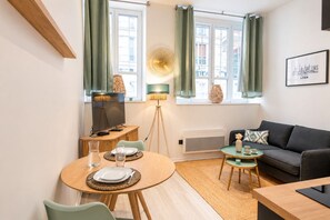 A modern living room with a sofa, a dining table with chairs, a television, and a floor lamp. - Opéra 2 - Lovely studio Hôtel de Ville (Lyon)