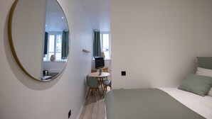 A modern bedroom with a large round mirror, a bed with green bedding, a small round table with chairs, and a TV on a stand. - Opéra 2 - Lovely studio Hôtel de Ville (Lyon)