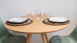 A round wooden table with two white plates, two clear glasses, and a clear glass pitcher. - Opéra 2 - Lovely studio Hôtel de Ville (Lyon)