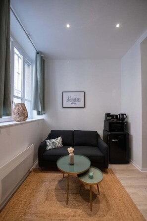 A modern living room with a black sofa, a small round table, a framed picture on the wall, and a window with curtains. - Opéra 2 - Lovely studio Hôtel de Ville (Lyon)