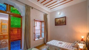 Un dormitorio con cama, ventana, un cuadro y un separador decorativo.