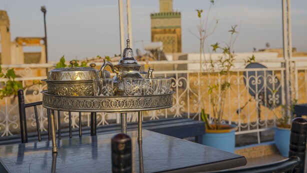 Una bandeja metálica con una tetera y vasos en un balcón con vista a una mezquita y al paisaje urbano.
