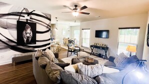 A living room with a sofa, a dining area, a ceiling fan, and a TV mounted on the wall. - Cheerful spacious home-5 min to Bruce's Field/Downtown (Aiken)