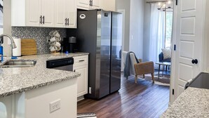A modern kitchen with white cabinets, a stainless steel refrigerator, and a granite countertop. - Cheerful spacious home-5 min to Bruce's Field/Downtown (Aiken)