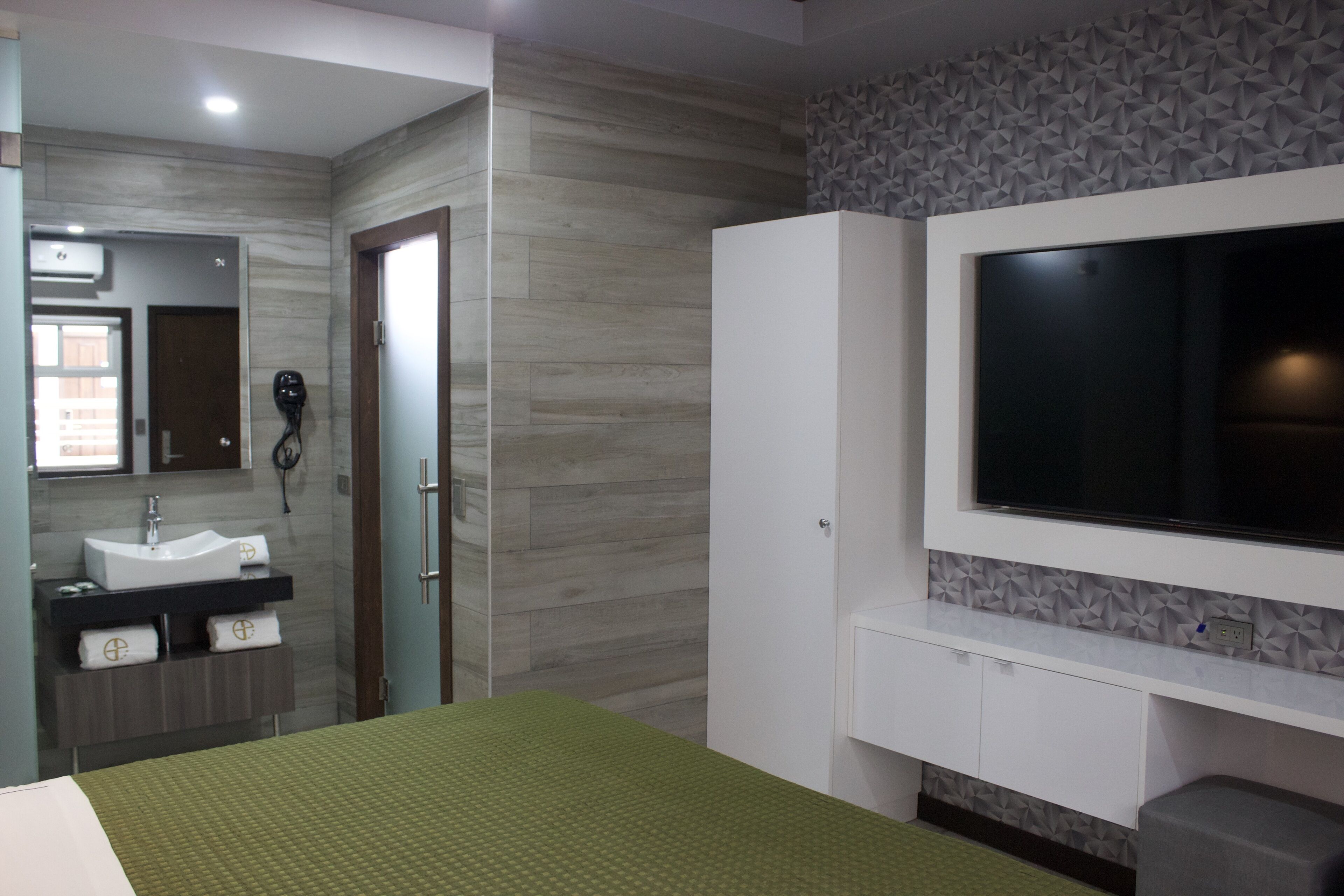 Une chambre d’hôtel moderne dotée d’un grand lit, d’un téléviseur intégré, d’une coiffeuse avec miroir et d’un téléphone fixé au mur.