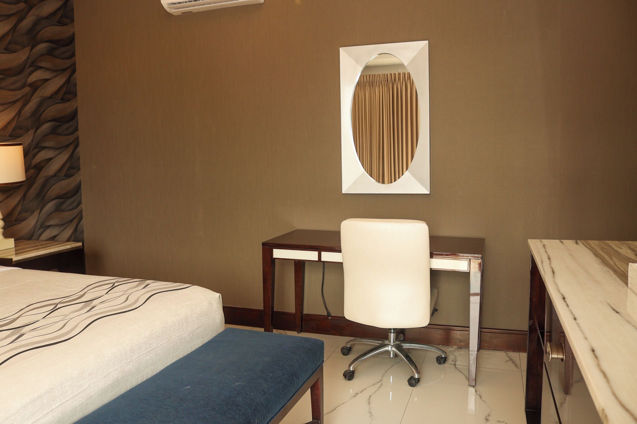A hotel room with a bed, a desk, a chair, and a wall-mounted air conditioner.