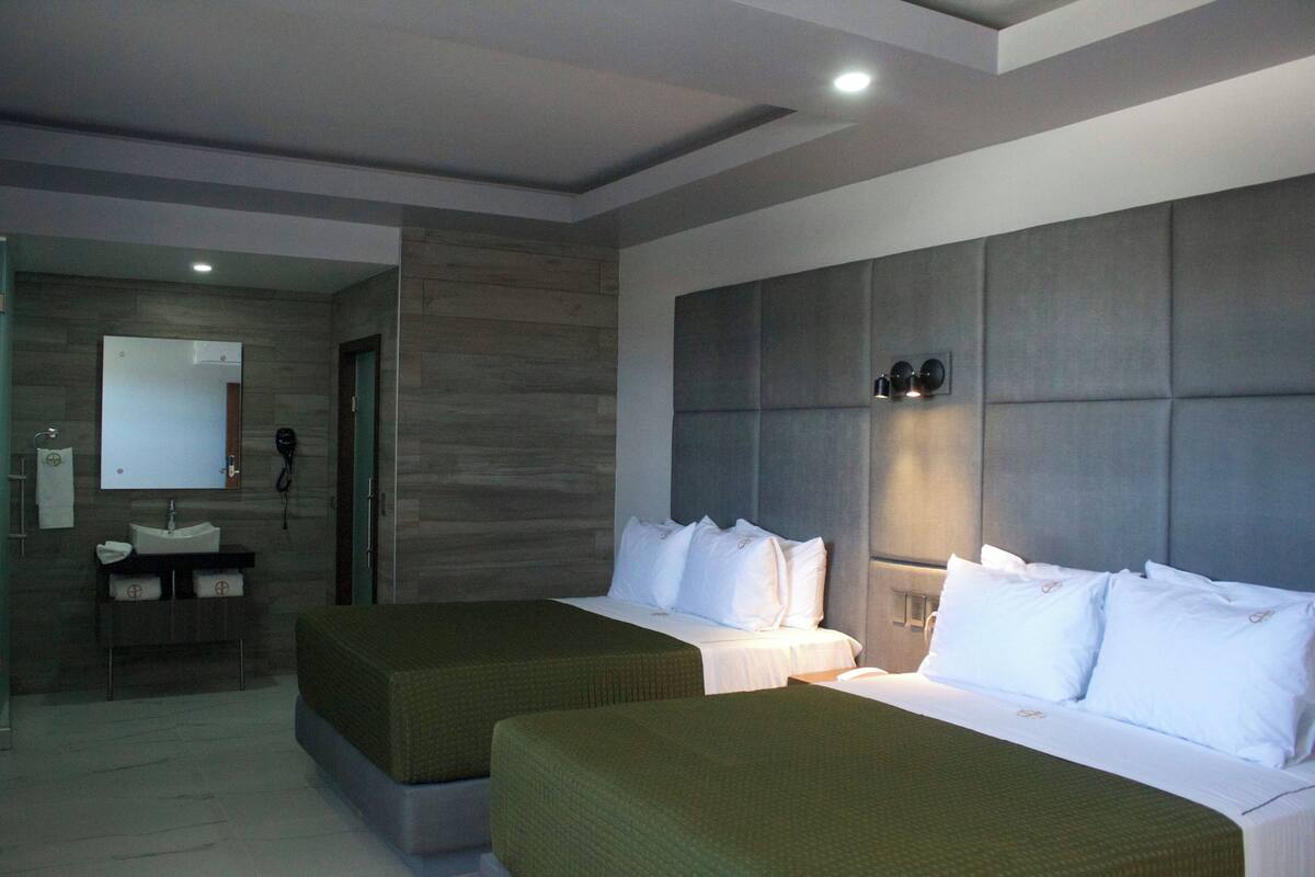 A hotel room with two beds, a large mirror, a vanity with a sink, and a door leading to another room.