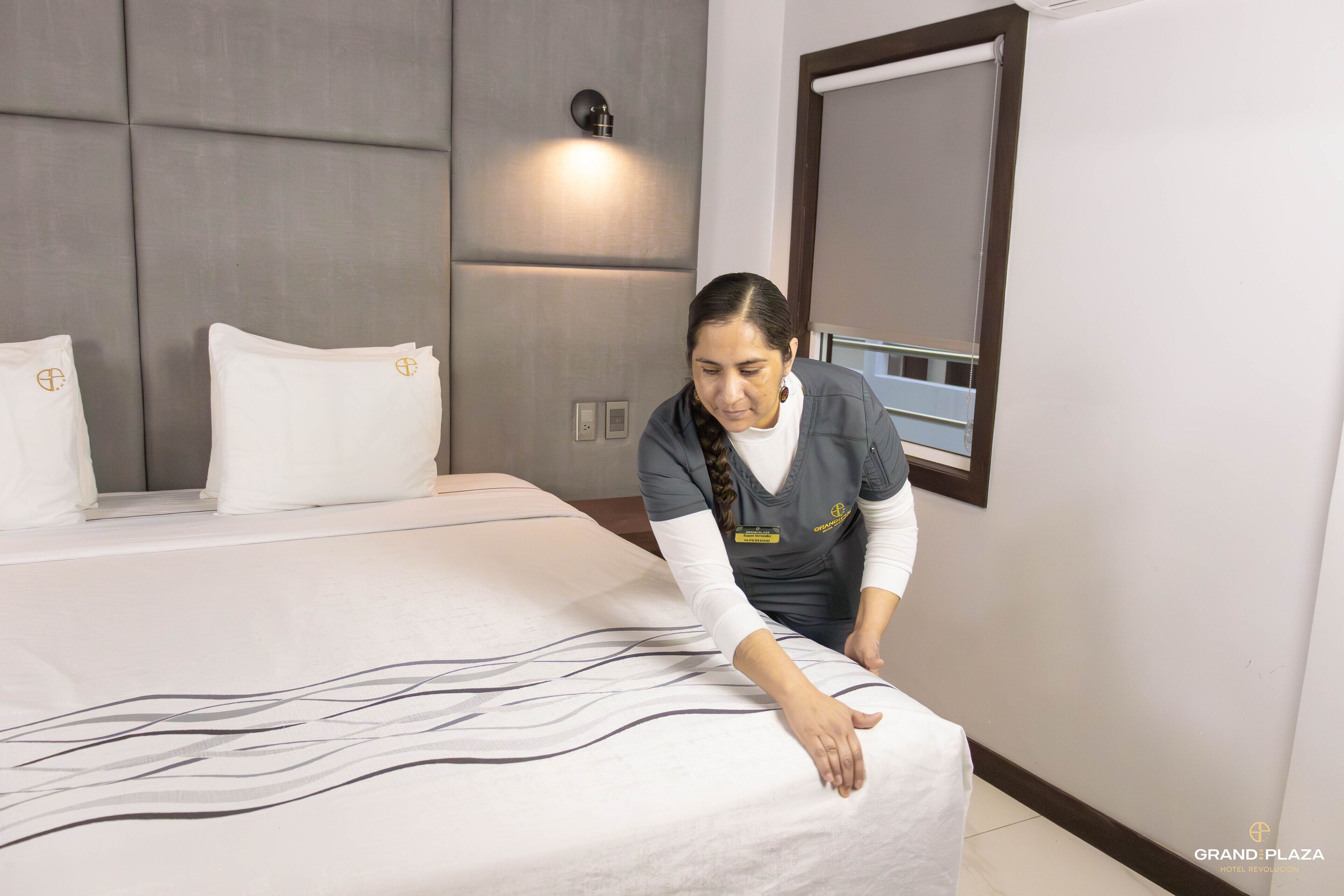 A hotel room with a neatly made bed, a wall-mounted light, and a large mirror.