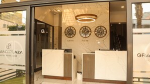 A reception area with marble walls, three clocks labeled 'Tijuana,' 'Madrid,' and 'New York,' and a modern reception desk. - Hotel Grand One Plaza (Tijuana)