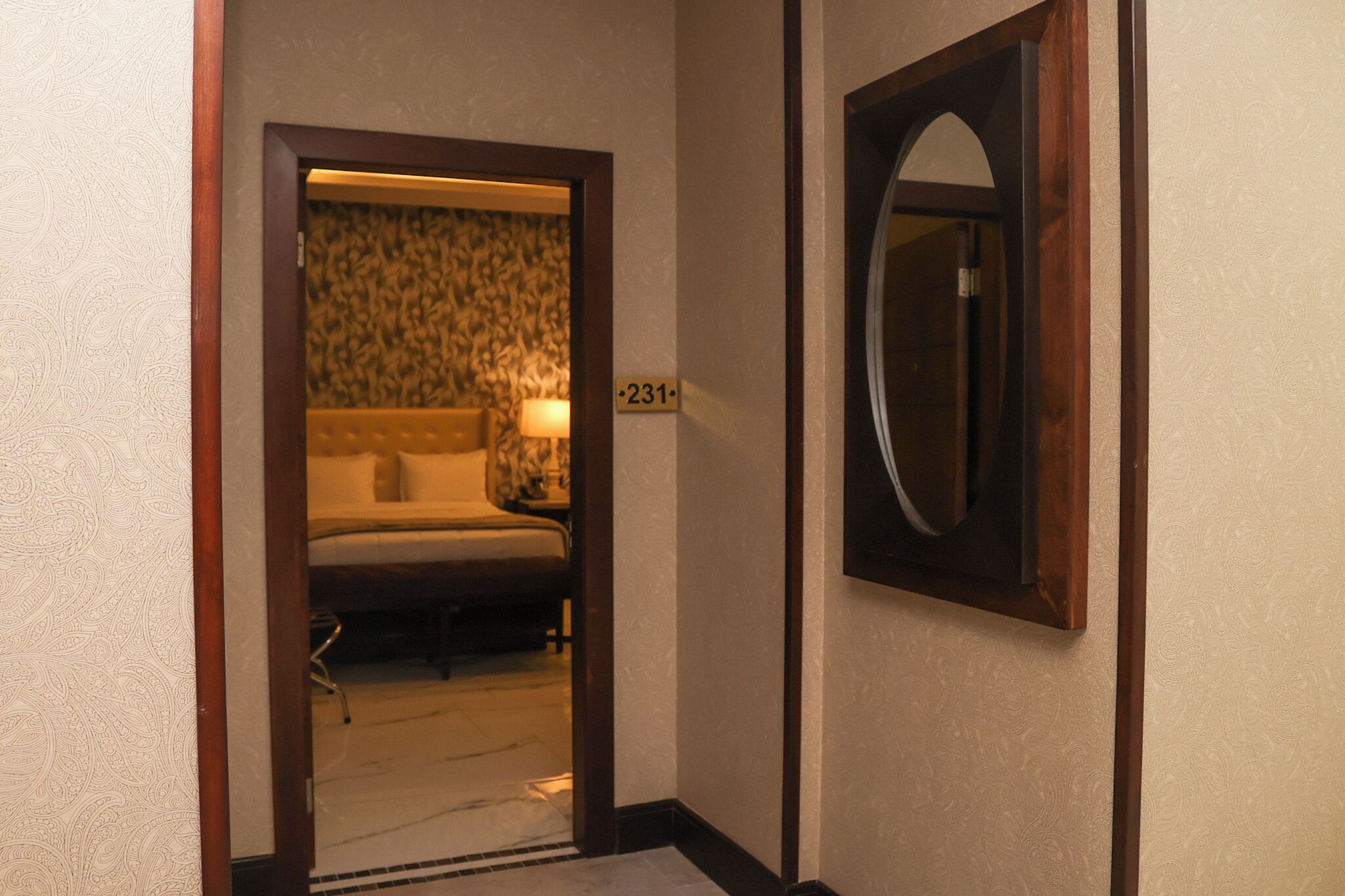 Een hotelkamer met een bed, nachtkastje, lamp en spiegel aan de muur.