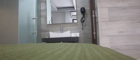A hotel room with a bed, a bathroom with a sink, a mirror, and a hairdryer.