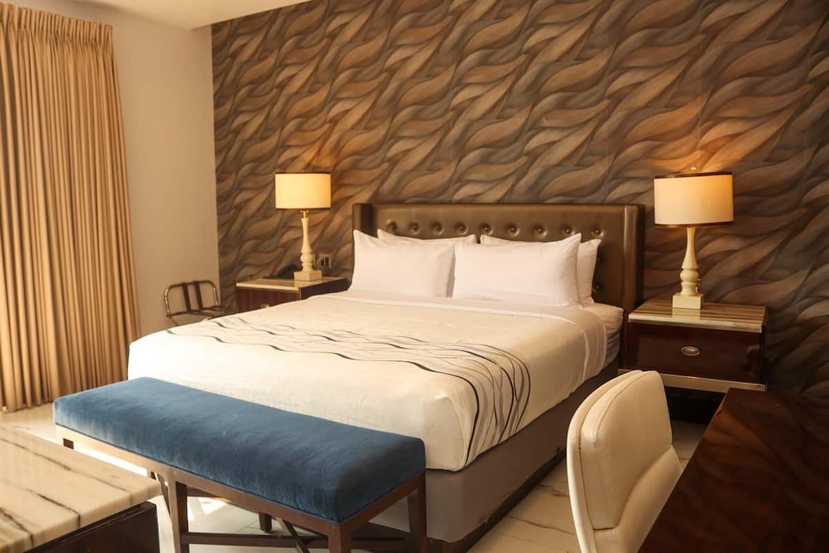 A hotel room with a bed, two bedside tables with lamps, a bench, and a chair.