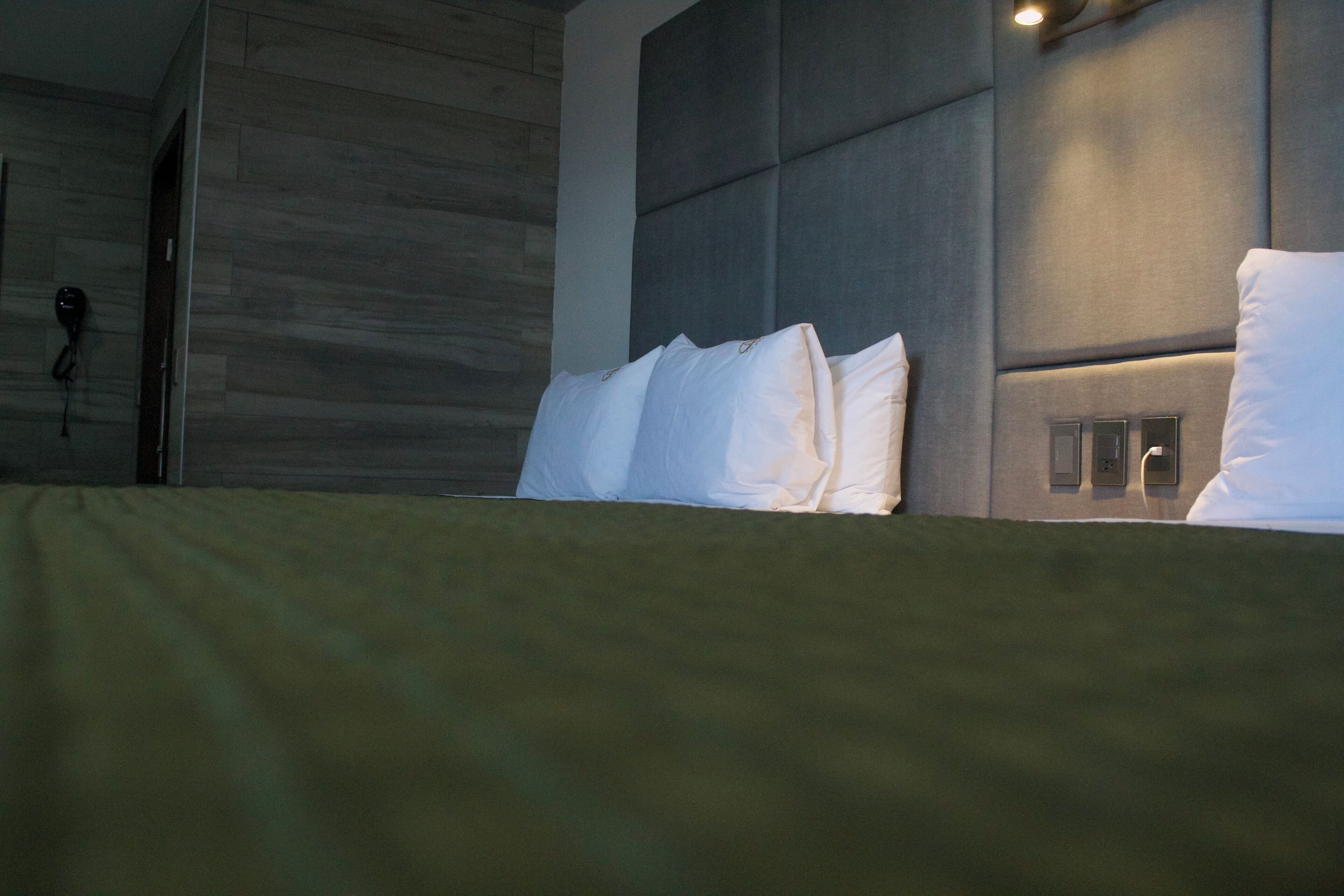 A modern hotel room with a large bed, a padded headboard, and a wall-mounted phone.