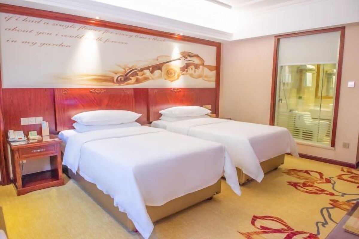 A hotel room with two beds, a wooden headboard, a small bedside table, and a floral carpet.