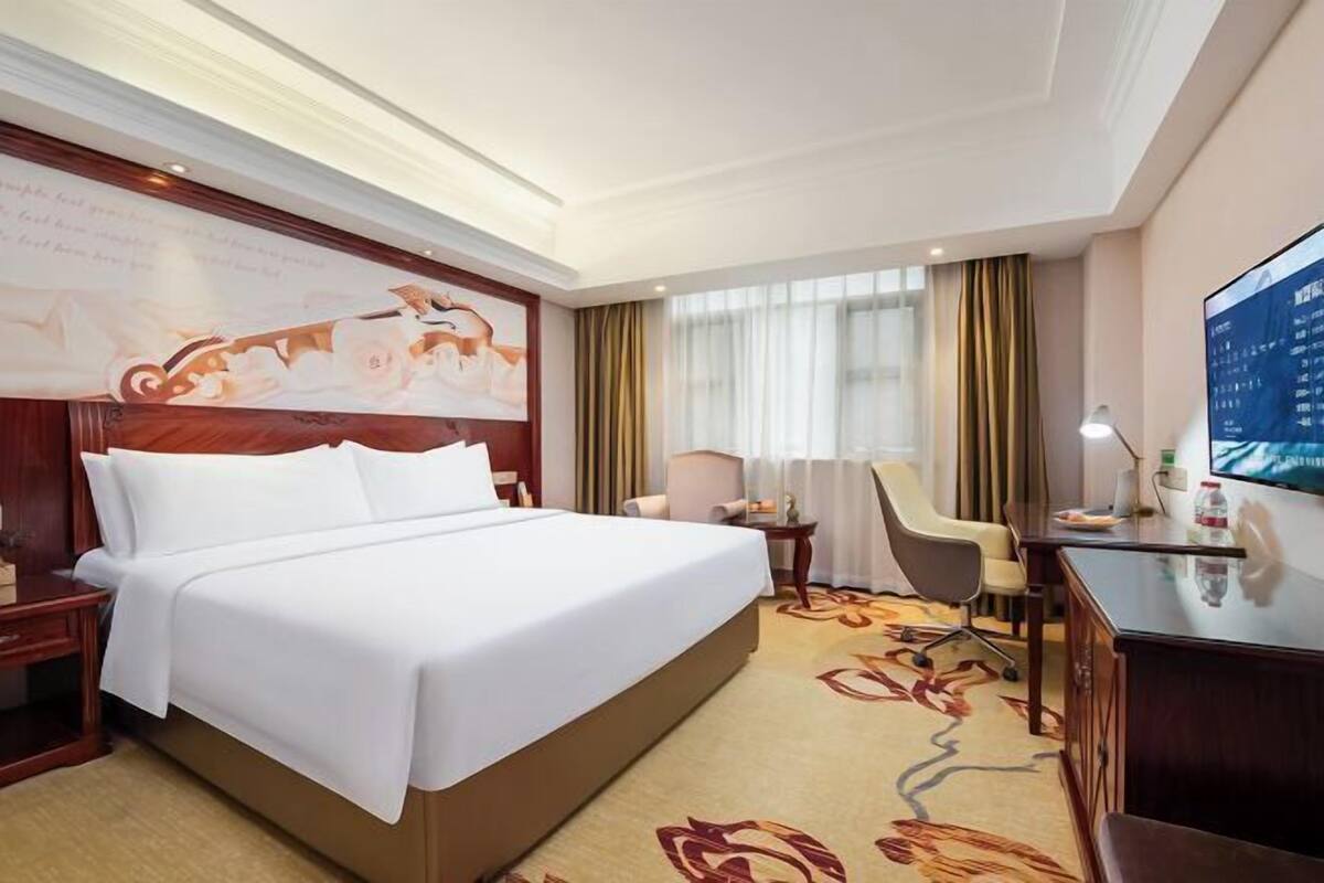 A hotel room with a large bed, a desk, a chair, and a TV.