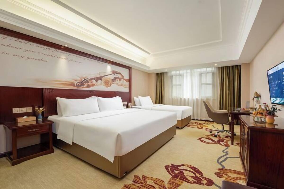 A hotel room with two beds, a desk, a chair, and a television.