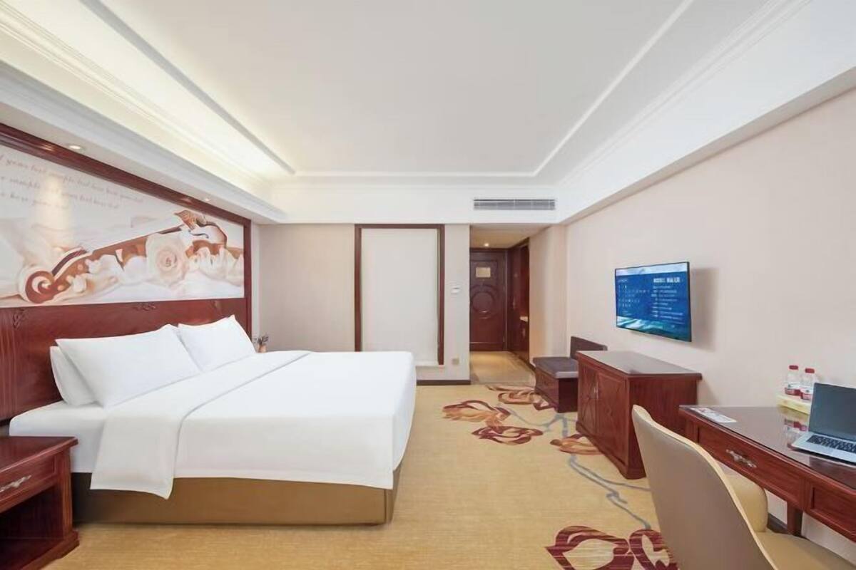 A hotel room with a bed, desk, chair, and a television on the wall.
