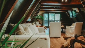Ein Schlafzimmer im Dachgeschoss mit Holzbalkendecke, einem weißen Sofa, einem Holzstuhl und einem großen Fenster.