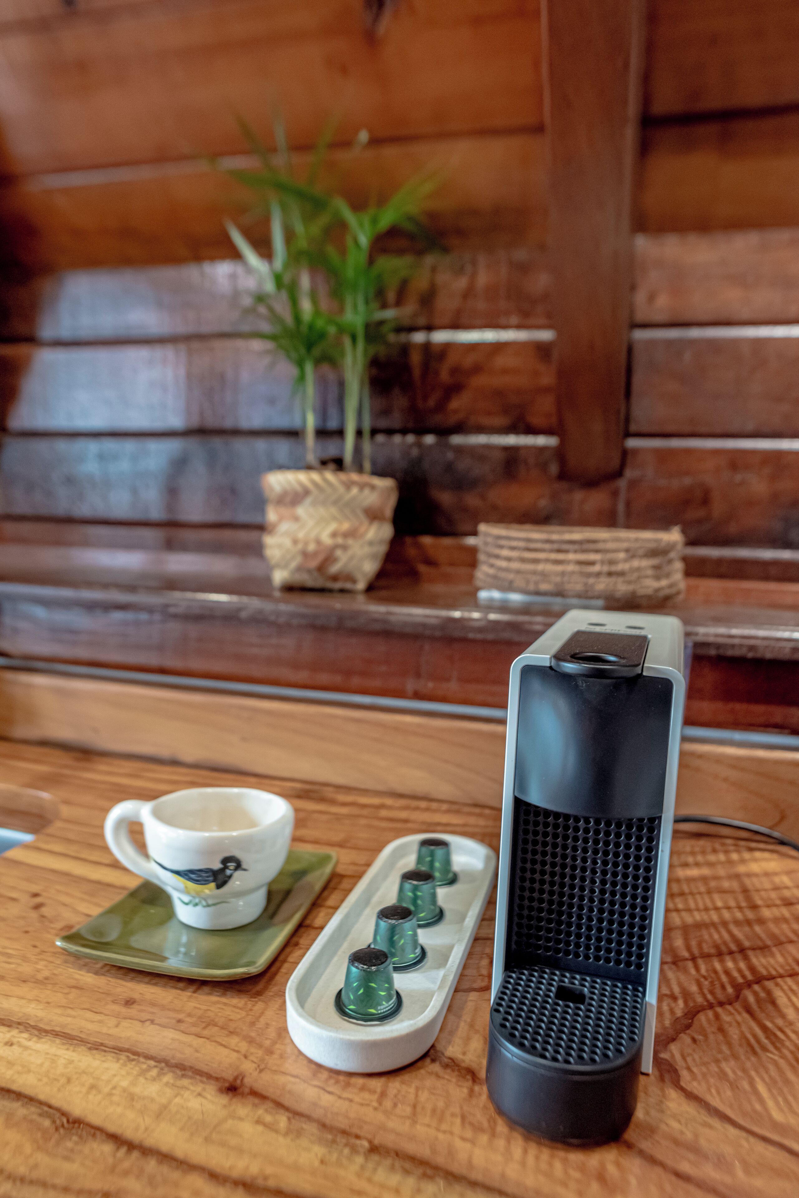 Una mesa de madera con una taza y platillo de cerámica blanca, una bandeja con objetos verdes y un altavoz negro.