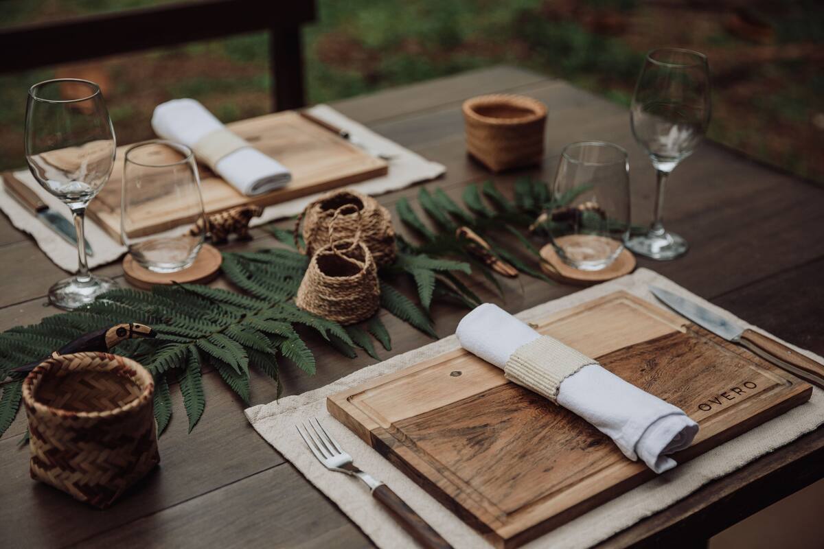 Une table en bois, mise avec des verres à vin, un couteau et une planche à découper portant l’inscription « Overo ».
