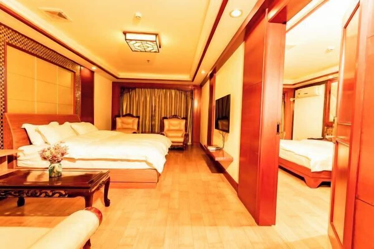 Una habitación de hotel con una cama grande, una cama más pequeña, un sofá, un televisor y suelo de madera.