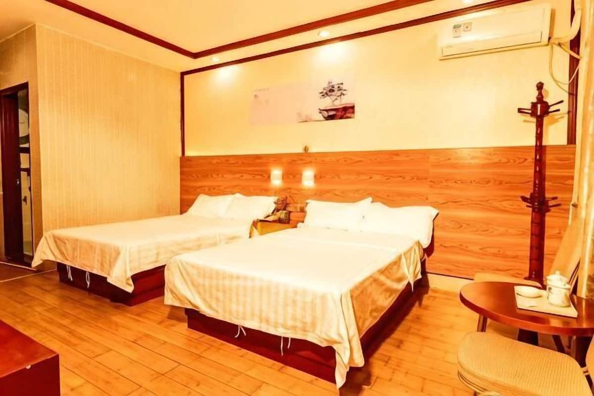 Habitación de hotel con dos camas, cabecero de madera, una mesita con una silla y aire acondicionado de pared.
