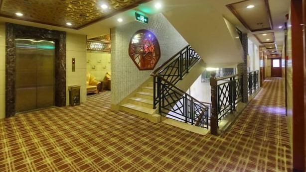 Een hotel lobby met een zwart-wit betegelde vloer, een trap met een zwarte leuning, en een decoratief plafond.