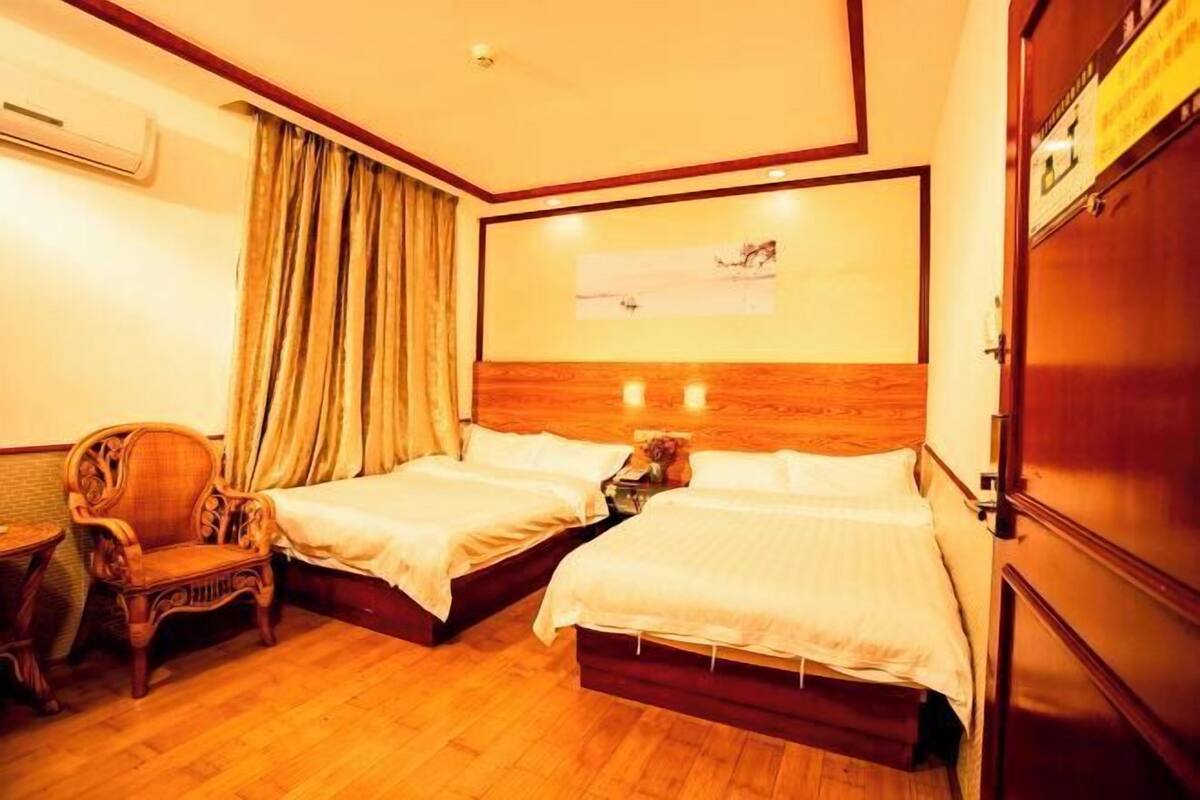 Habitación de hotel con dos camas, una silla de madera, un armario de madera y aire acondicionado instalado en la pared.