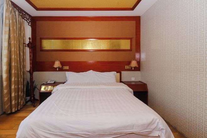 Een hotelkamer met een groot bed, twee nachtkastjes, een spiegel en een gordijn.