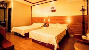 Een hotelkamer met twee bedden, houten vloeren, een tafeltje en een wandairconditioner.