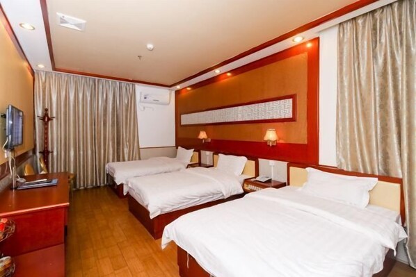 Een hotelkamer met drie eenpersoonsbedden, een houten bureau, een televisie en een wandairconditioning.