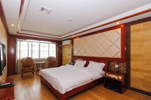 A hotel room with a large bed, a wooden headboard, a desk, and a chair. - Hepu Dongyuan Hotel (Hepu)