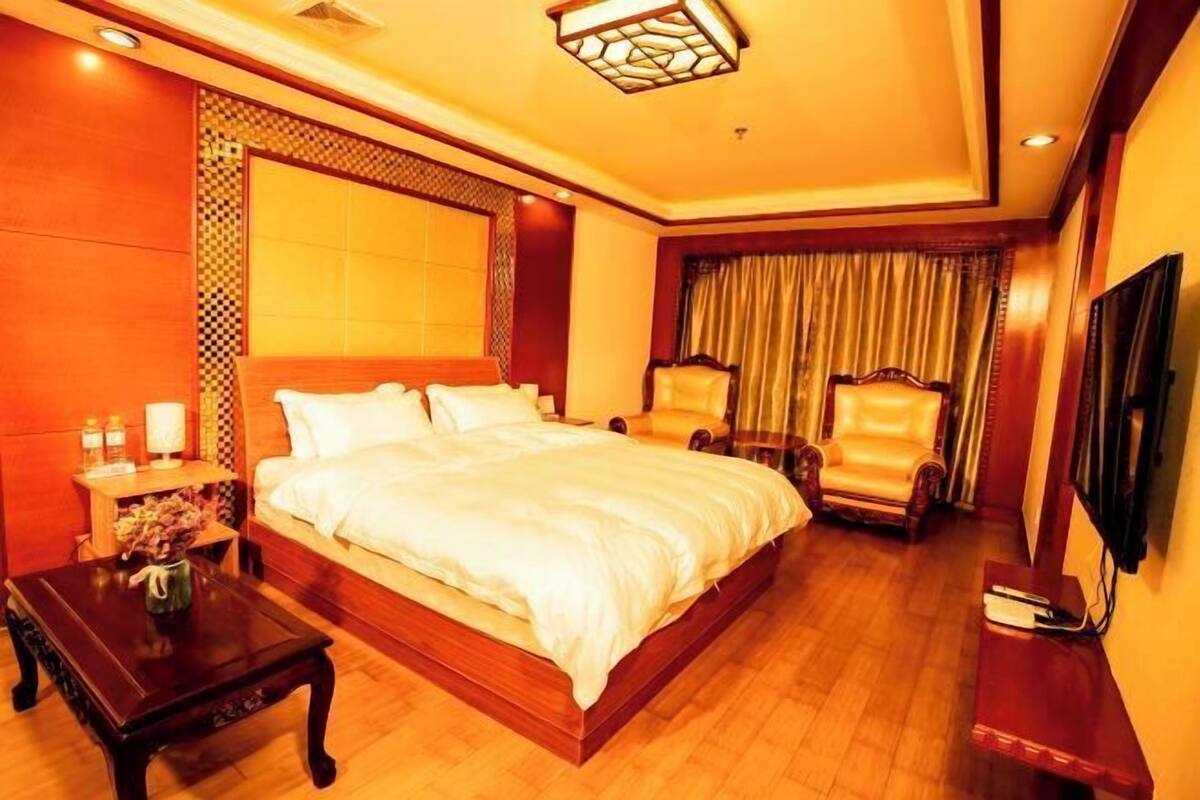 Una habitación de hotel con una cama grande, dos sillones, un televisor y piso de madera.