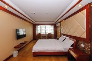 A hotel room with a large bed, a television, a small table, and a window with a view.