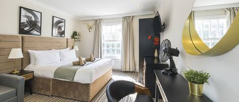 A hotel room with a bed, bedside table, lamp, chair, desk, potted plant, and a large mirror.