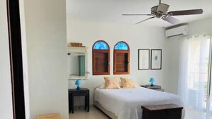 A bedroom with a bed, a ceiling fan, a nightstand, a small wooden stool, and a window with a view. - Encanto- 2 Bedroom Beachfront Condo - Simpson Bay! (Simpson Bay)