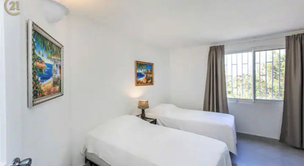Una habitación de hotel con dos camas, una ventana con cortinas y dos cuadros en las paredes.