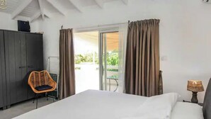 Un dormitorio con cama, una silla, un armario y un balcón con cortinas.