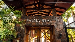 Fachada de piedra con puerta de madera y un cartel que dice "POSADA PALMA REAL IGUIAZÚ".