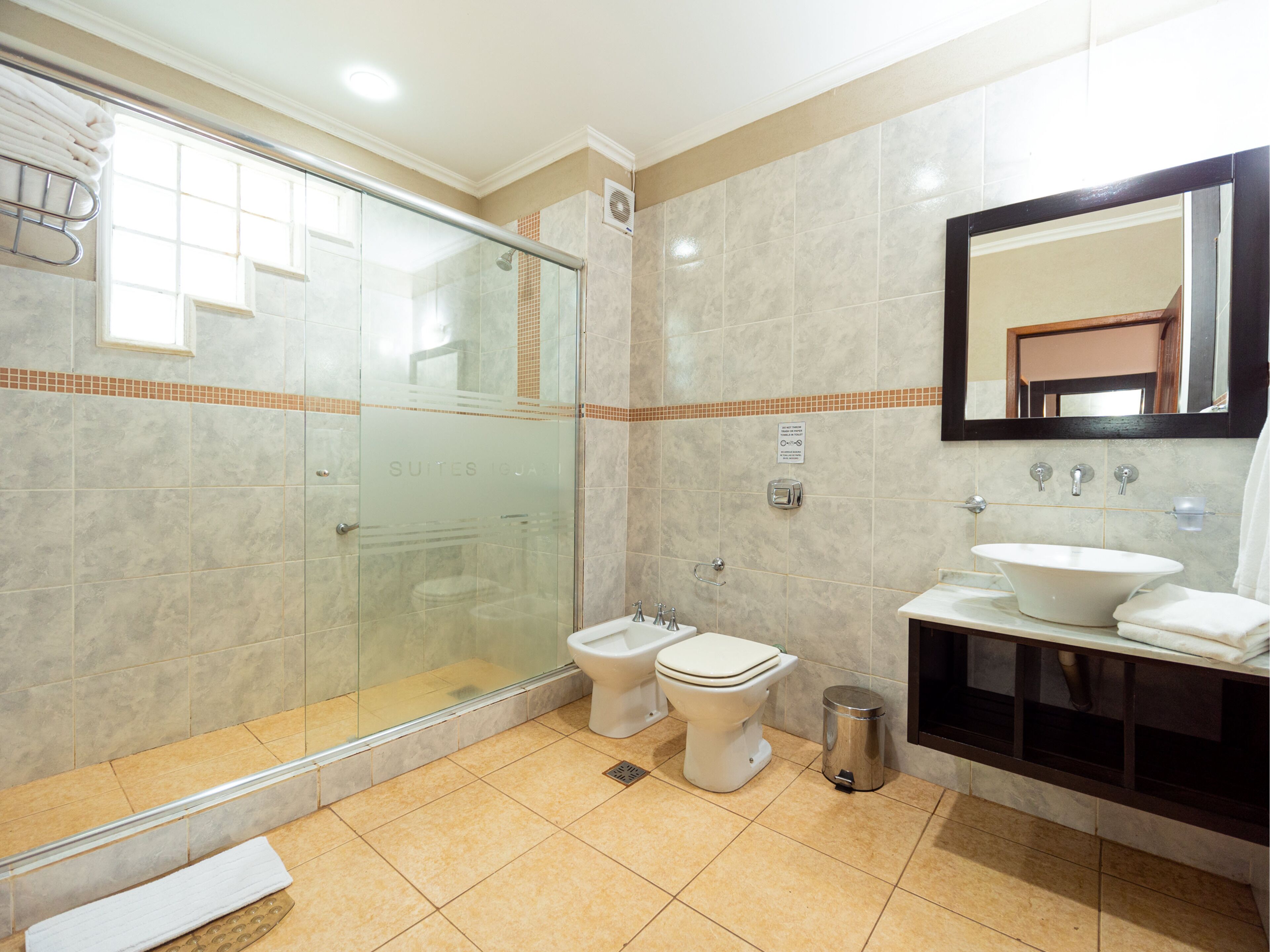 Ein modernes Badezimmer mit einer gläsernen Duschkabine, zwei Toiletten, einem Waschbecken und einem Mülleimer.