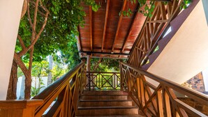 Una escalera de madera con barandilla de metal que conduce a una zona techada con vistas al follaje exterior.
