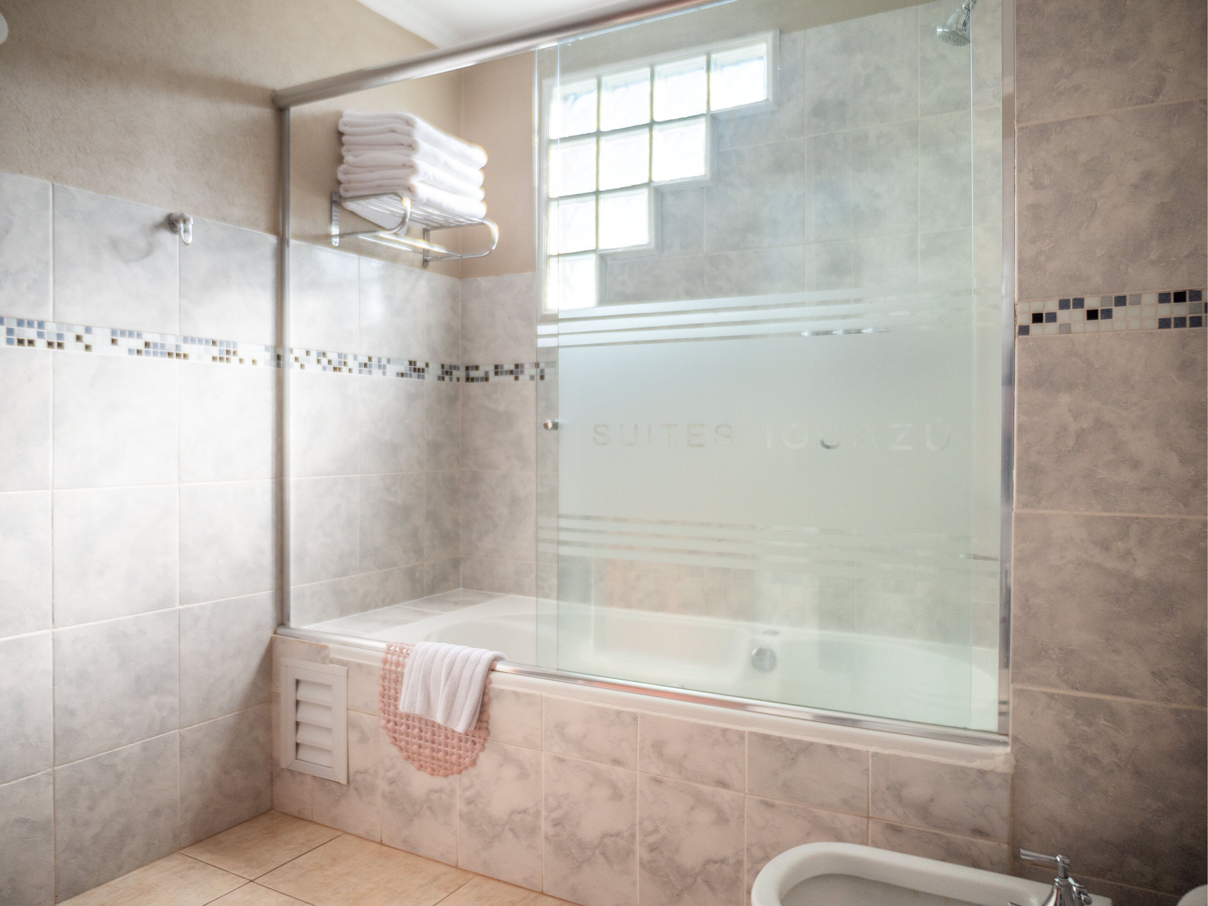 Un baño moderno con cabina de ducha de vidrio, un banco integrado y un perchero para toallas.