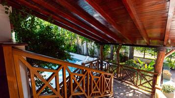 A wooden balcony with a view of a swimming pool and lush greenery.