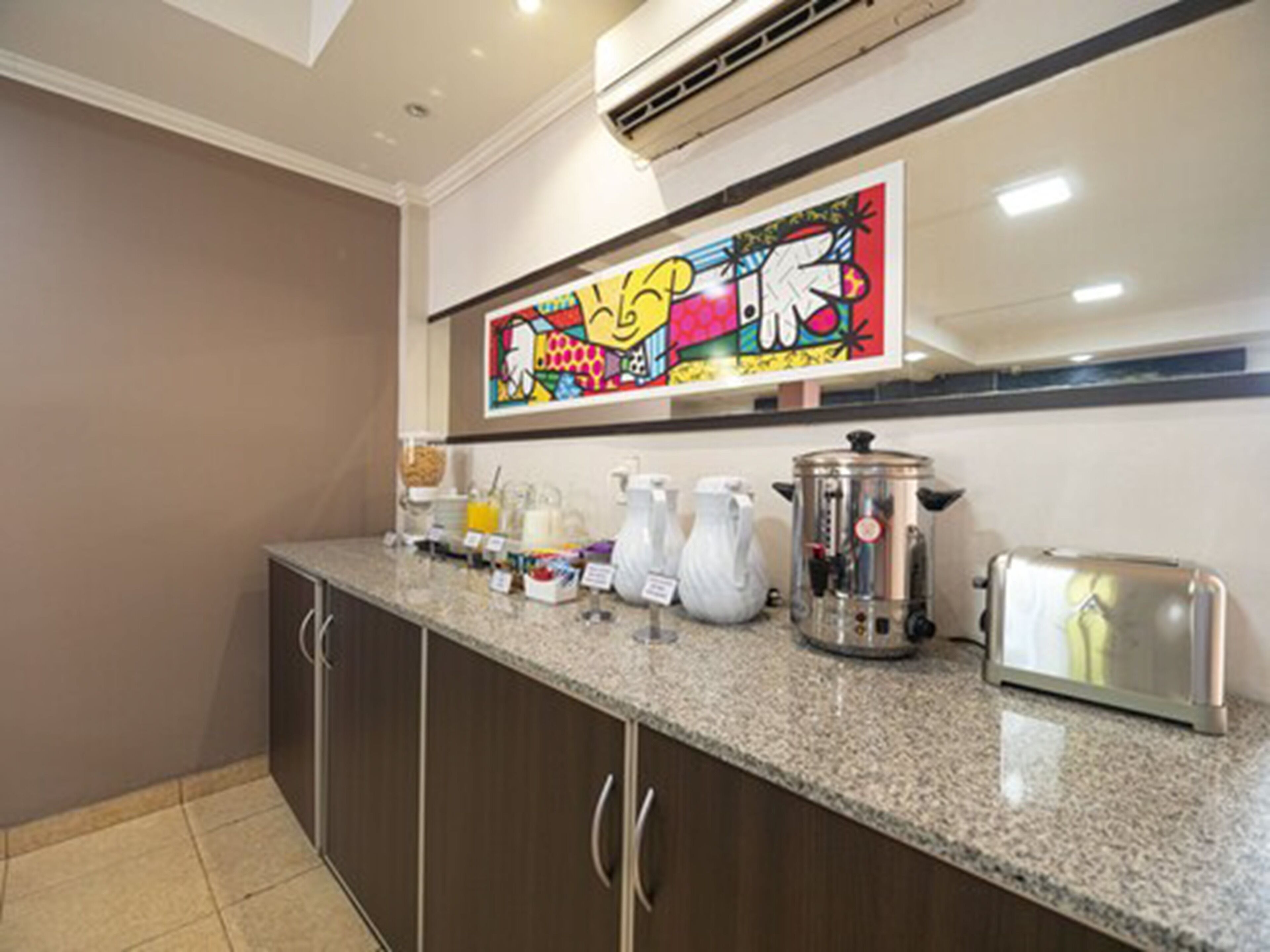 A kitchen with a granite countertop, stainless steel appliances, and a colorful artwork above the sink.