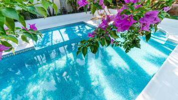 A clear blue pool surrounded by lush greenery and white lounge chairs.