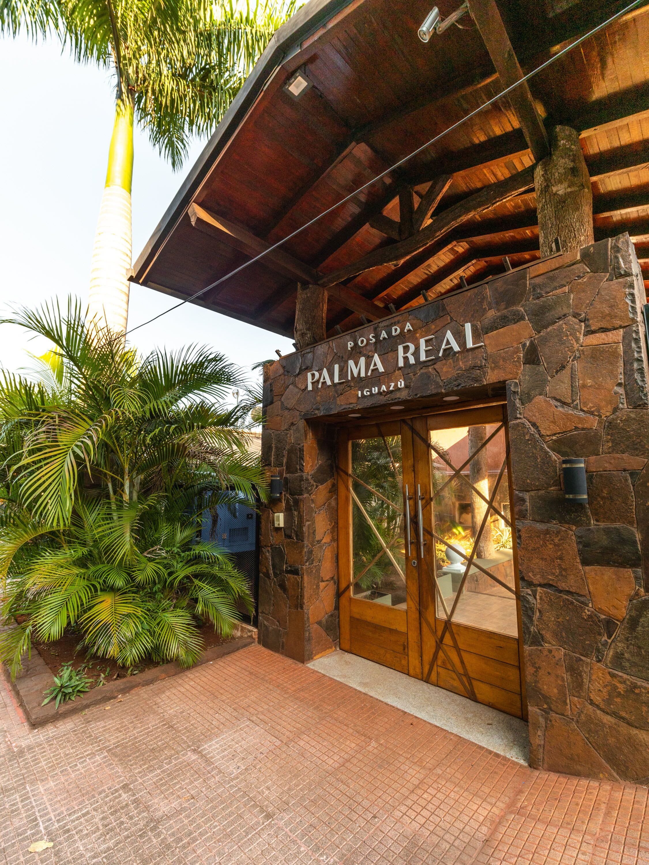 The exterior of Palma Real hotel with stone walls, a wooden entrance, and tropical plants.