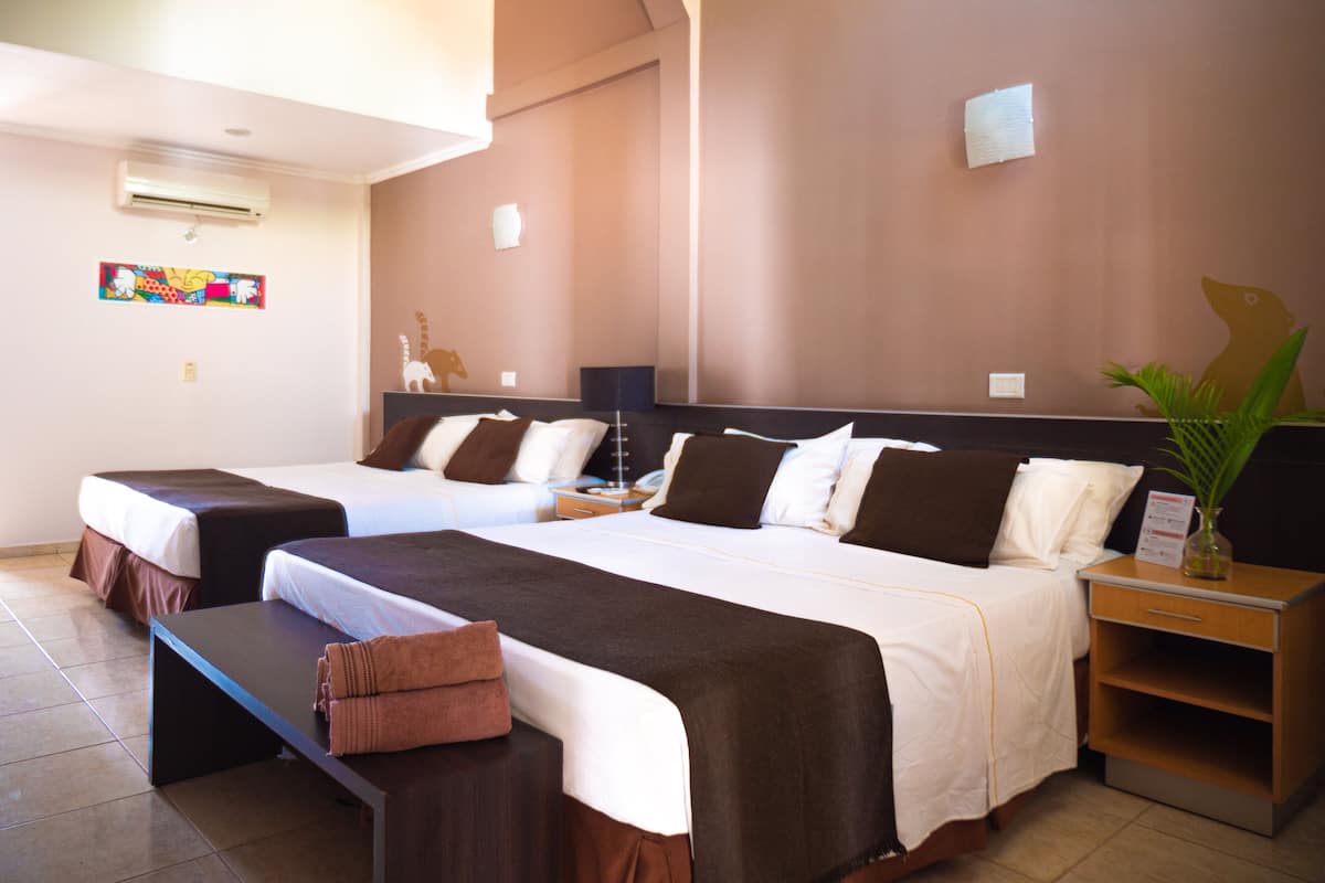 Quarto de hotel com duas camas, uma escrivaninha, uma mesa de cabeceira e uma pequena planta.