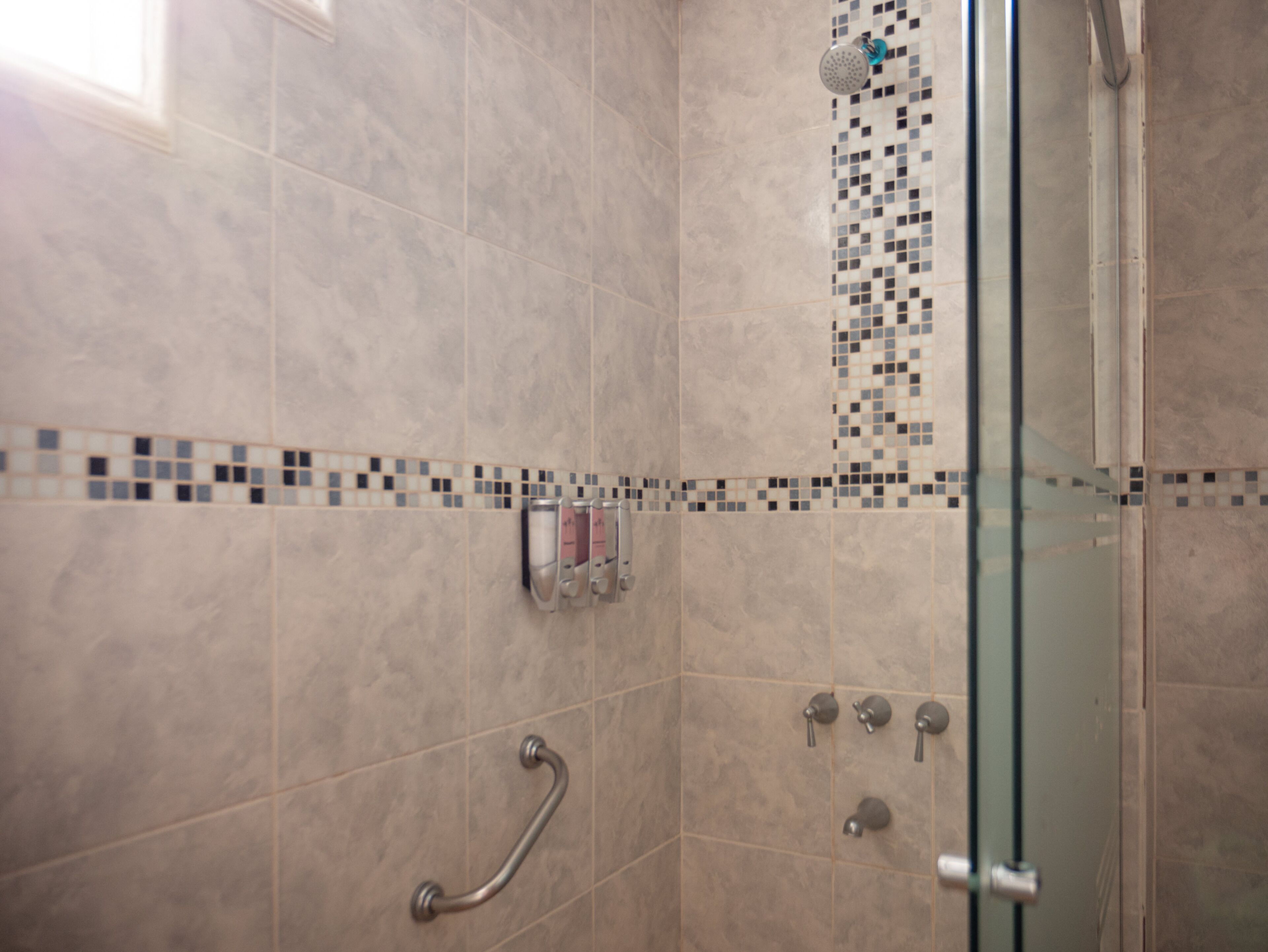 Un espace douche doté d’une porte en verre, d’une barre d’appui et d’un pare-feu en mosaïque.